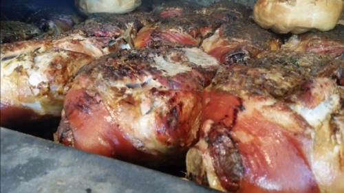 Close-up of several roasted pork hocks, golden brown and crispy, with smoky charred edges.