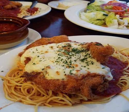 A plate of spaghetti topped with marinara sauce, fried chicken, melted cheese, and garnished with parsley.