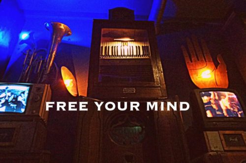 A vintage display with musical instruments, old TVs, and a glowing hand, featuring the text "FREE YOUR MIND."