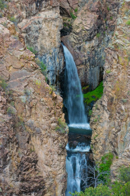 A waterfall cascading through rocky cliffs, surrounded by lush greenery and rugged terrain.