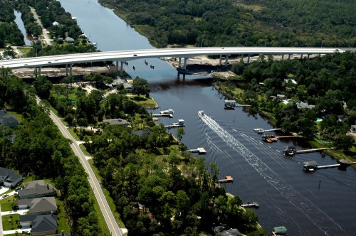 Aerial view of a river with boats, a highway bridge, and lush greenery along the banks.