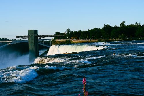A view of Niagara Falls with cascading water, surrounded by greenery and a clear blue sky.