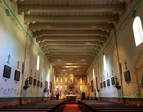 Interior of a church featuring wooden beams, colorful altar, and decorative walls with artwork and religious symbols.