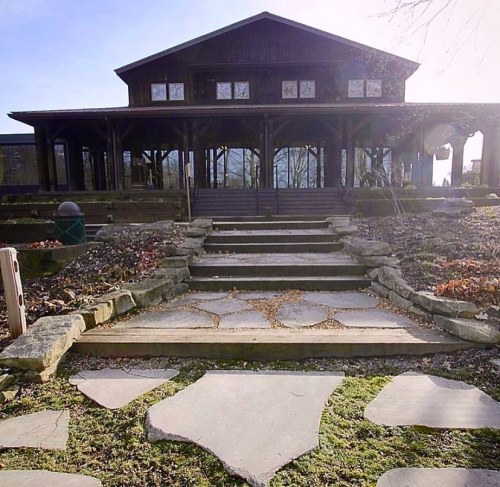 A stone pathway leads to a large, dark wooden building with multiple windows and a landscaped garden.