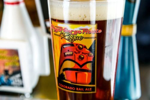 A glass of Colorado Rail Ale with a colorful label featuring a train design and a frothy top.