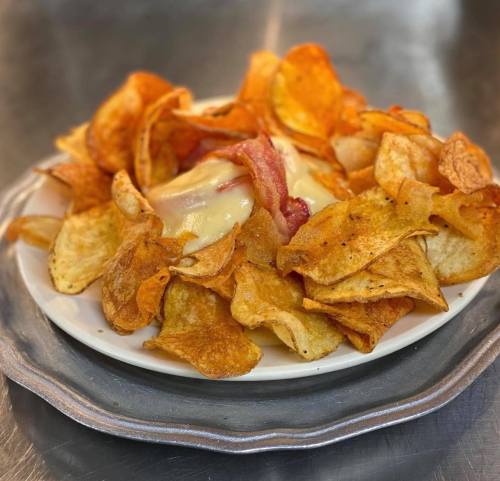 A plate of crispy potato chips topped with melted cheese and bits of bacon, served on a silver platter.