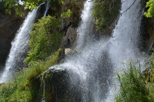 A scenic view of multiple waterfalls cascading over rocky cliffs, surrounded by lush greenery and mist.