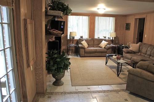 Cozy living room with beige sofas, a coffee table, plants, and large windows letting in natural light.