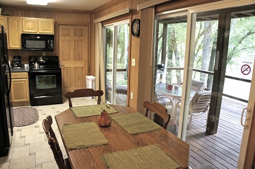 Cozy kitchen with wooden cabinets, a dining table set for four, and sliding doors leading to a deck surrounded by trees.