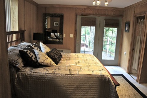 Cozy bedroom with a large bed, decorative pillows, wooden walls, and sliding glass doors leading to an outdoor area.