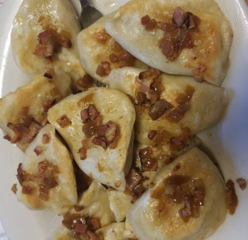 A plate of golden-brown pierogi topped with crispy bacon bits.