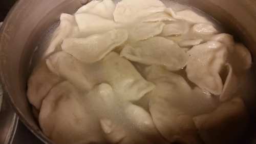 A pot of boiling water filled with dumplings, partially submerged and steaming.