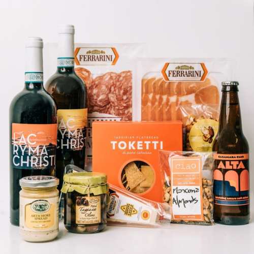 A selection of gourmet food items including wine, meats, spreads, and snacks arranged on a white background.