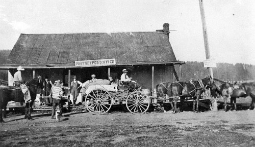 Historic black-and-white photo of a post office with people and horse-drawn wagons outside.