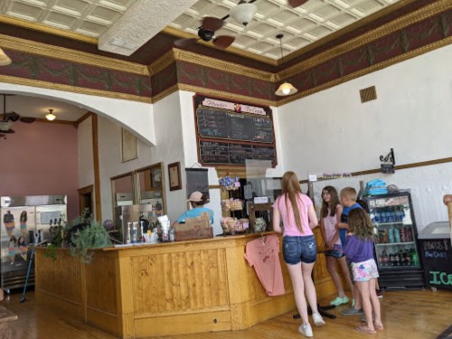 A cozy ice cream shop with a wooden counter, a menu board, and customers ordering at the counter.
