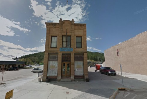 Historic building with a decorative facade, surrounded by a small town and mountains under a partly cloudy sky.