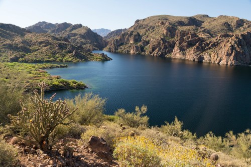 A serene lake surrounded by rocky hills and lush greenery under a clear blue sky.