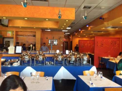 A brightly colored restaurant interior with buffet trays, tables set for dining, and a staff member in the background.