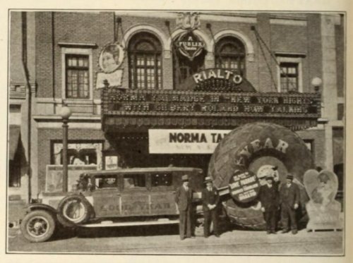 Historic photo of the Rialto Theatre with a large Goodyear tire and a vintage car parked outside.