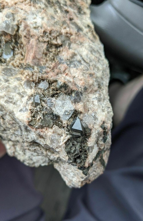 Close-up of a rough rock with shiny black and clear crystal formations embedded in it.