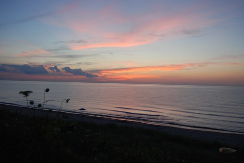 A serene beach at sunset, with soft pink and orange hues reflecting on calm waters and gentle waves.