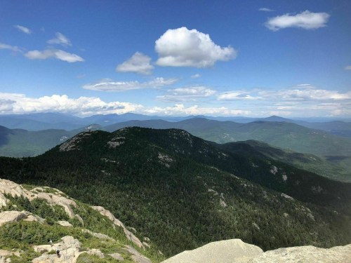 A panoramic view of green mountains under a blue sky with fluffy clouds, showcasing a serene natural landscape.