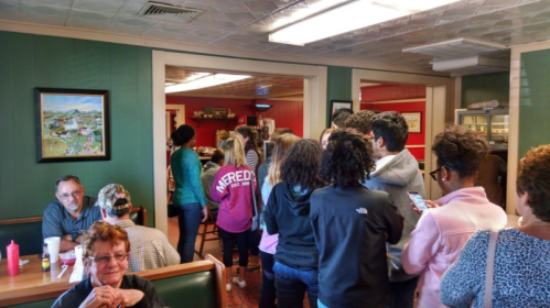 A busy diner scene with a line of people waiting to order, while others are seated at tables.