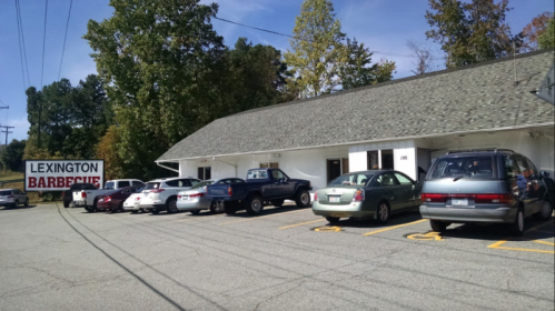 A barbecue restaurant with a sign reading "Lexington Barbecue" and a parking lot filled with various cars.