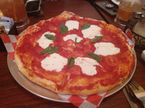 A freshly baked pizza topped with tomato sauce, mozzarella cheese, and fresh basil leaves on a wooden table.