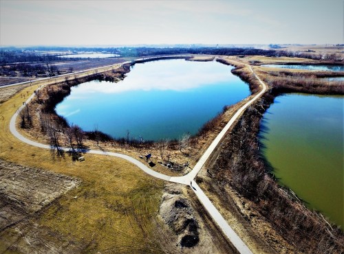 Aerial view of a winding water body surrounded by land, with a path along the shore and trees in the background.