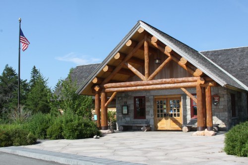 A rustic building with a log cabin design, featuring a stone facade and a flagpole, surrounded by greenery.
