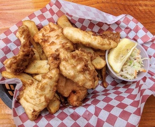 A basket of fried fish fillets and golden fries, served with a lemon wedge and a side of coleslaw.