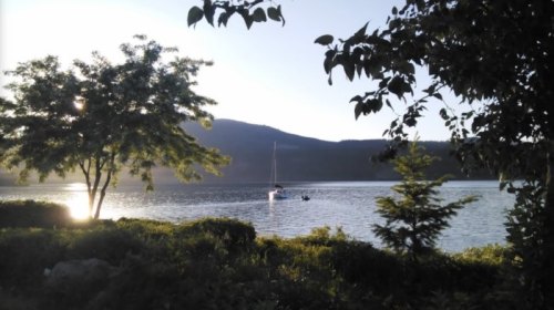 A serene lake scene with a sailboat, surrounded by trees and mountains under a clear sky.