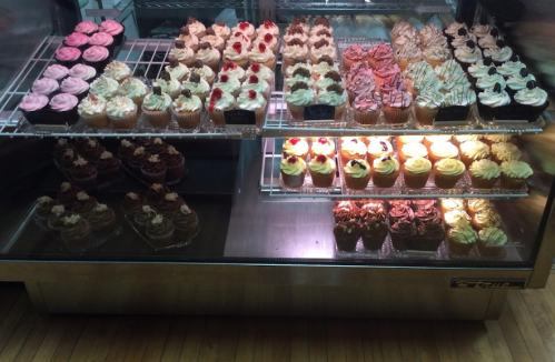 A display case filled with an assortment of colorful cupcakes, featuring various frosting styles and toppings.