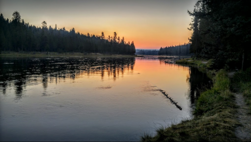 A serene river at sunset, surrounded by trees, with vibrant colors reflecting on the water's surface.