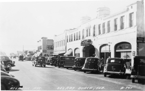 Black and white photo of Atlantic Avenue in Delray Beach, Florida, featuring vintage cars and historic buildings.