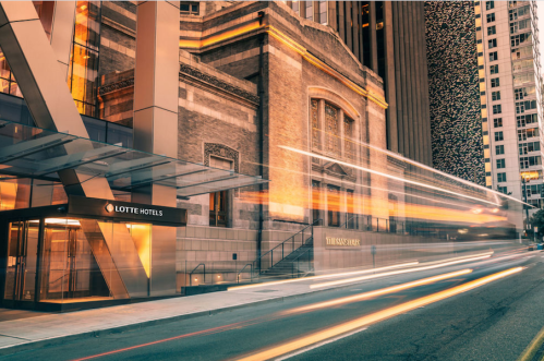 Lotte Hotels entrance with a historic building backdrop, illuminated at night, and light trails from passing vehicles.