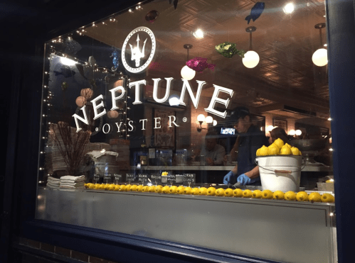 A restaurant window displays the name "Neptune Oyster" with a chef preparing food inside, surrounded by decorative lights.