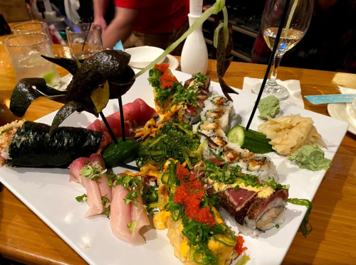 A vibrant sushi platter featuring various rolls, sashimi, and garnishes, served on a white plate.