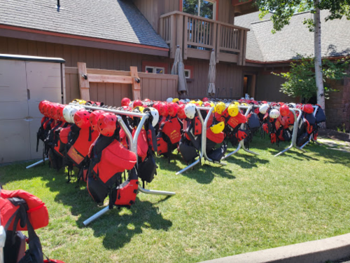 A row of red and yellow life jackets hanging on a rack outside a building, with green grass in the foreground.