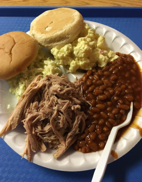 A plate with pulled pork, baked beans, potato salad, and two sandwich buns on a blue tray.