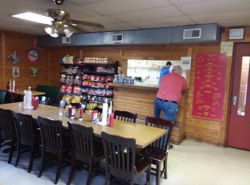 A cozy diner interior with a long table, chairs, snack shelves, and staff preparing food in the background.