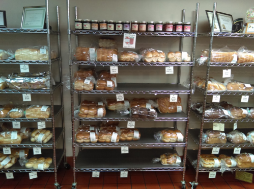 Shelves filled with various types of bread and jars of jam, all neatly labeled and displayed in a bakery.