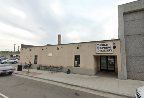 Exterior of Cold Spring Bakery, featuring a light-colored building with outdoor seating and a sign above the entrance.
