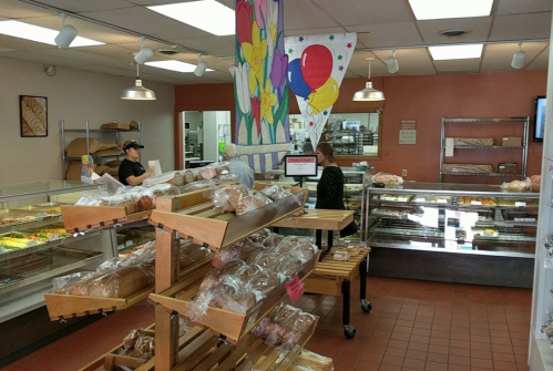 A bakery interior with shelves of bread, a colorful mural, and two customers interacting near the display cases.