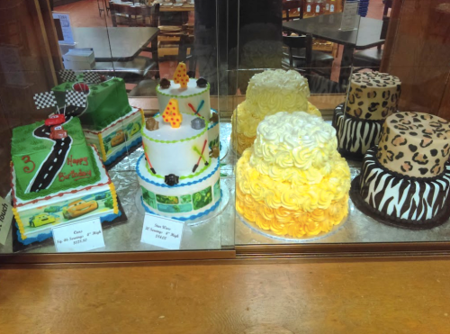 A display of colorful cakes, including a race car theme, a tiered cake with decorations, and patterned round cakes.