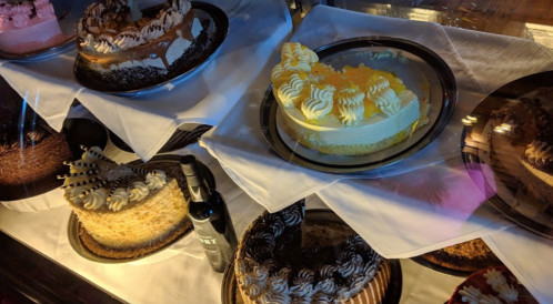 A display of various cakes, including layered and frosted options, with a bottle of wine beside them.