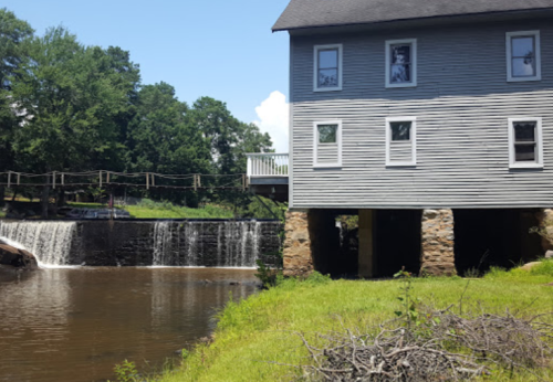 A historic building beside a small waterfall, with lush greenery and a clear blue sky in the background.