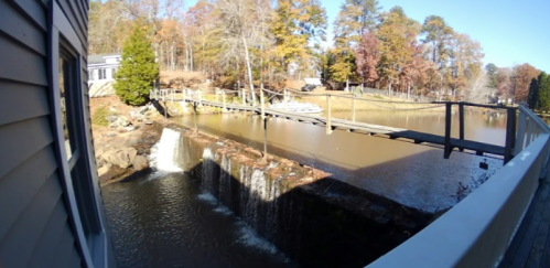 A serene view of a small waterfall flowing into a calm lake, with a wooden bridge crossing over the water.