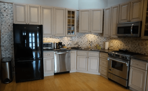 Modern kitchen featuring light cabinets, stainless steel appliances, and a tiled backsplash. Hardwood floor visible.